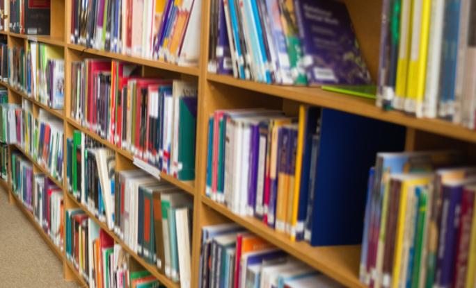 Eine Studentin nimmt sich ein Buch aus dem Bücherregal (c) Fotolia / Wavebreakmedia Redhead student taking book from shelf in the library at the university