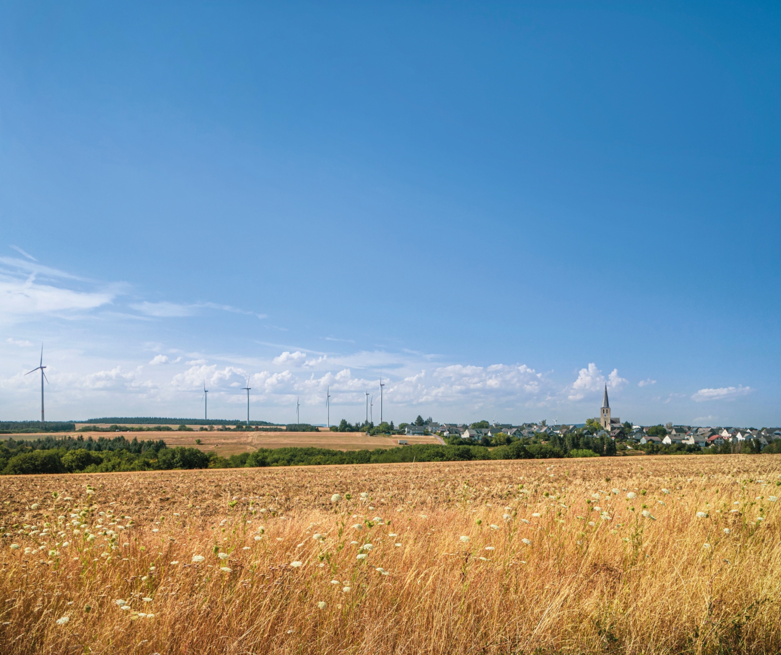 Wind turbines as an renewable energy concept and a harvested field at the town of moersfeld in the palatine region in Germany